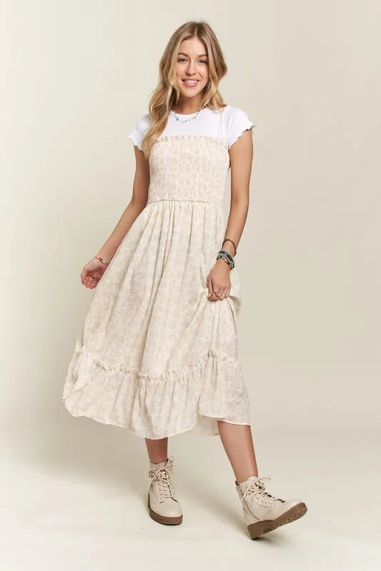 Woman wearing a smocked floral cami dress with a ruffled hem in beige and white.