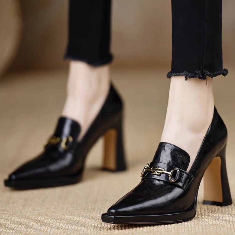 A pair of black pointed toe chunky heel pumps with gold hardware on a neutral background