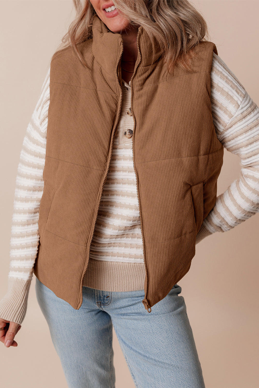 Woman wearing a brown cropped corduroy stand neck puffer vest with a front zip closure