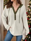 Close up front view of a woman wearing a cream waffle-knit hoodie with a dark olive green buttoned placket and hood