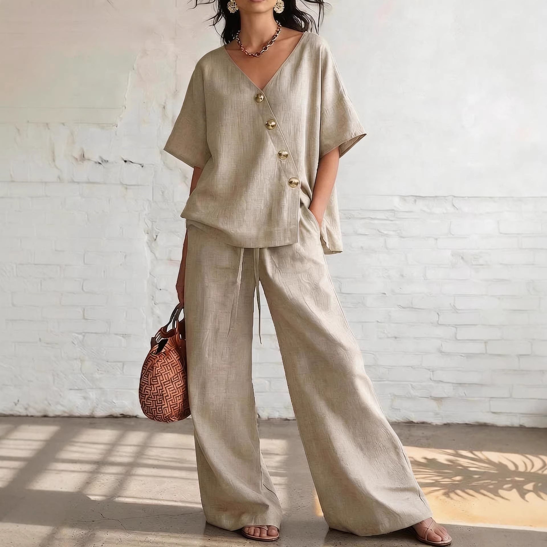 Woman wearing a beige cotton-linen V-neck short-sleeve top with diagonal button closure and matching wide-leg pants.