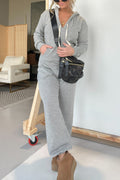 Woman wearing a comfortable grey long sleeve hooded jumpsuit with a drawstring waist and side pockets.