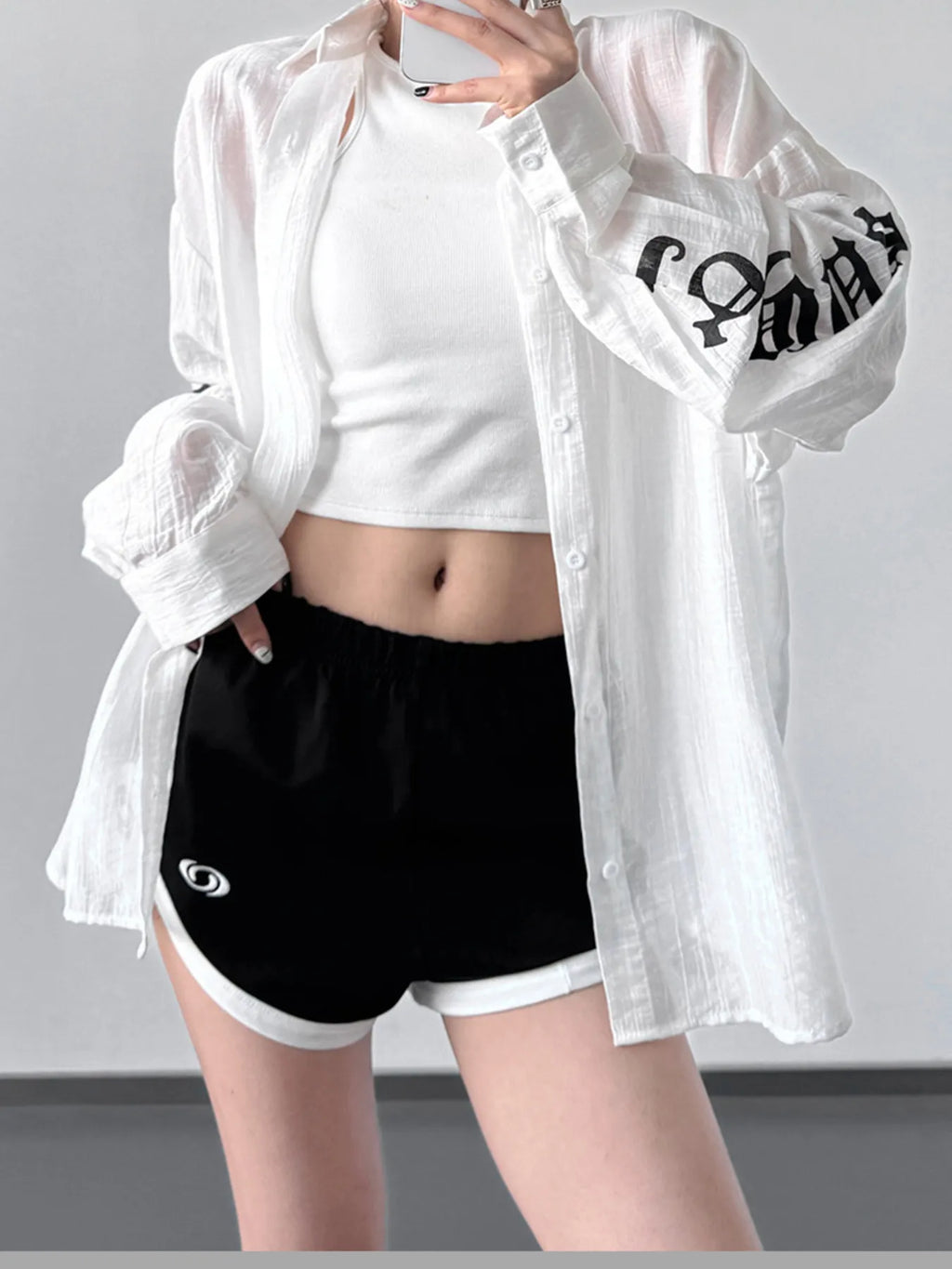A woman wearing a white, oversized sheer long sleeve button-up shirt layered over a white tank top.