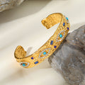 Gold tone stainless steel open cuff bracelet featuring a central turquoise-colored eye with zircon stone accents