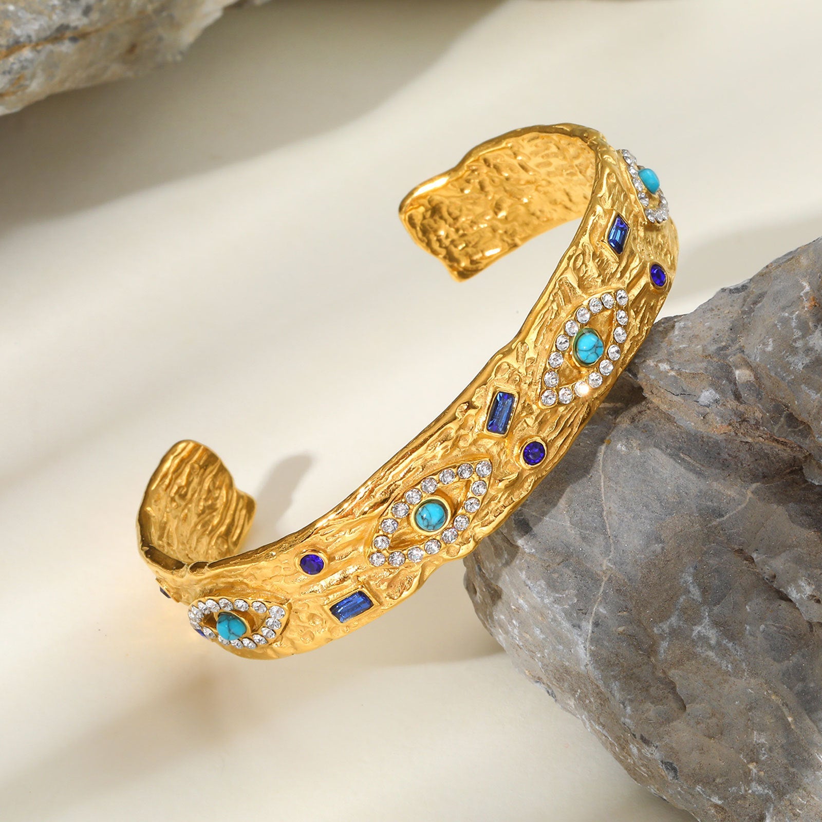 Gold tone stainless steel open cuff bracelet featuring a central turquoise-colored eye with zircon stone accents