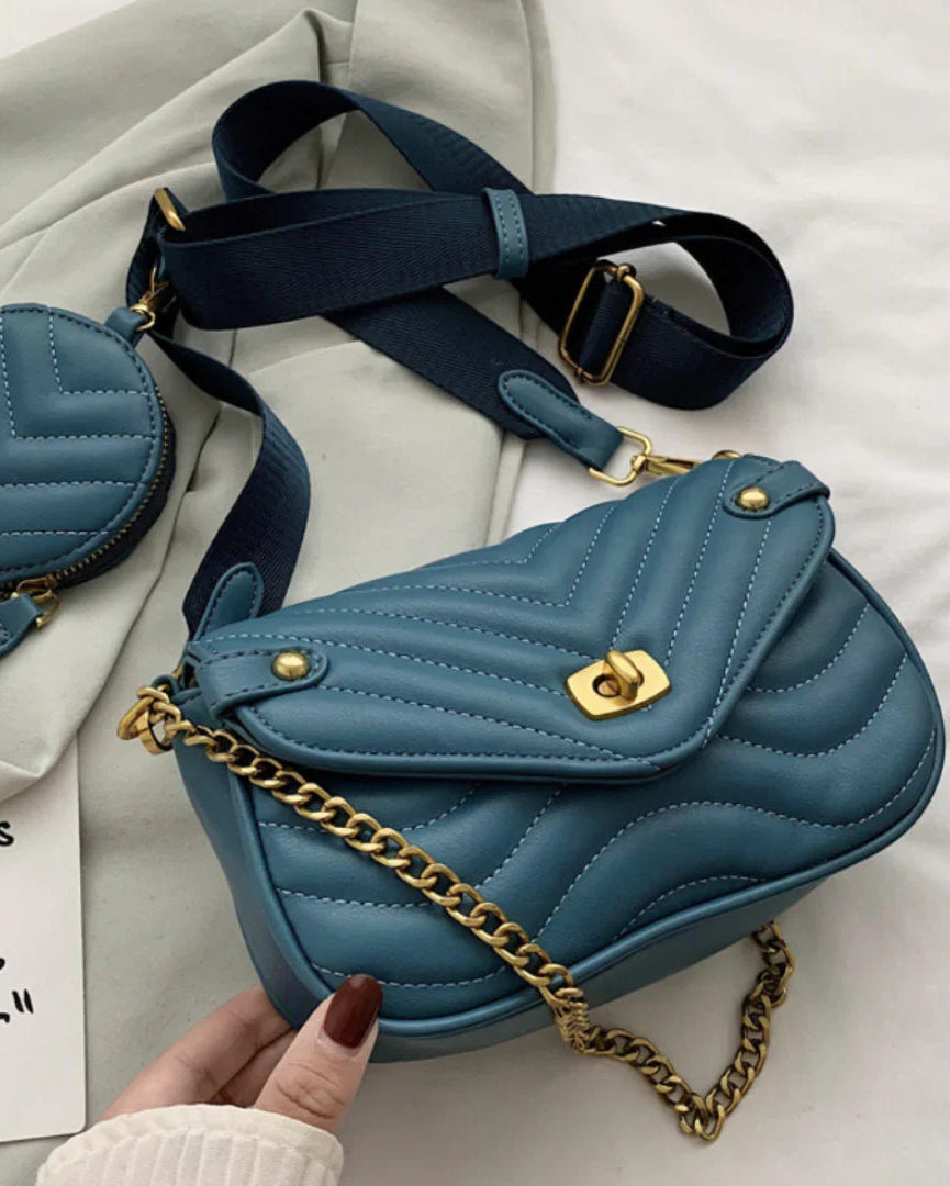 Blue quilted handbag with gold chain and matching round pouch on a light background