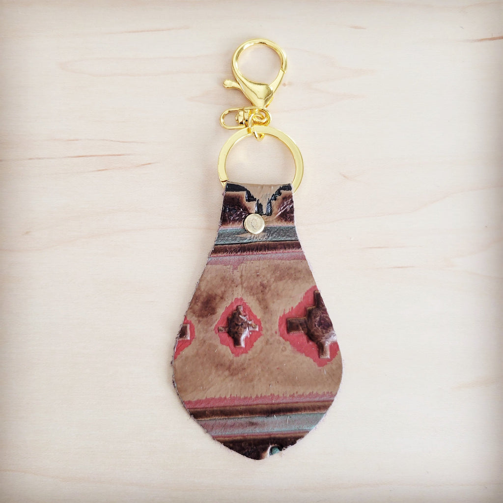A leather keychain with a red and brown Navajo-inspired geometric print and gold-tone metal hardware against a light wooden background.