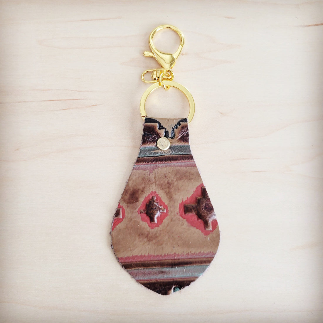 A leather keychain with a red and brown Navajo-inspired geometric print and gold-tone metal hardware against a light wooden background.