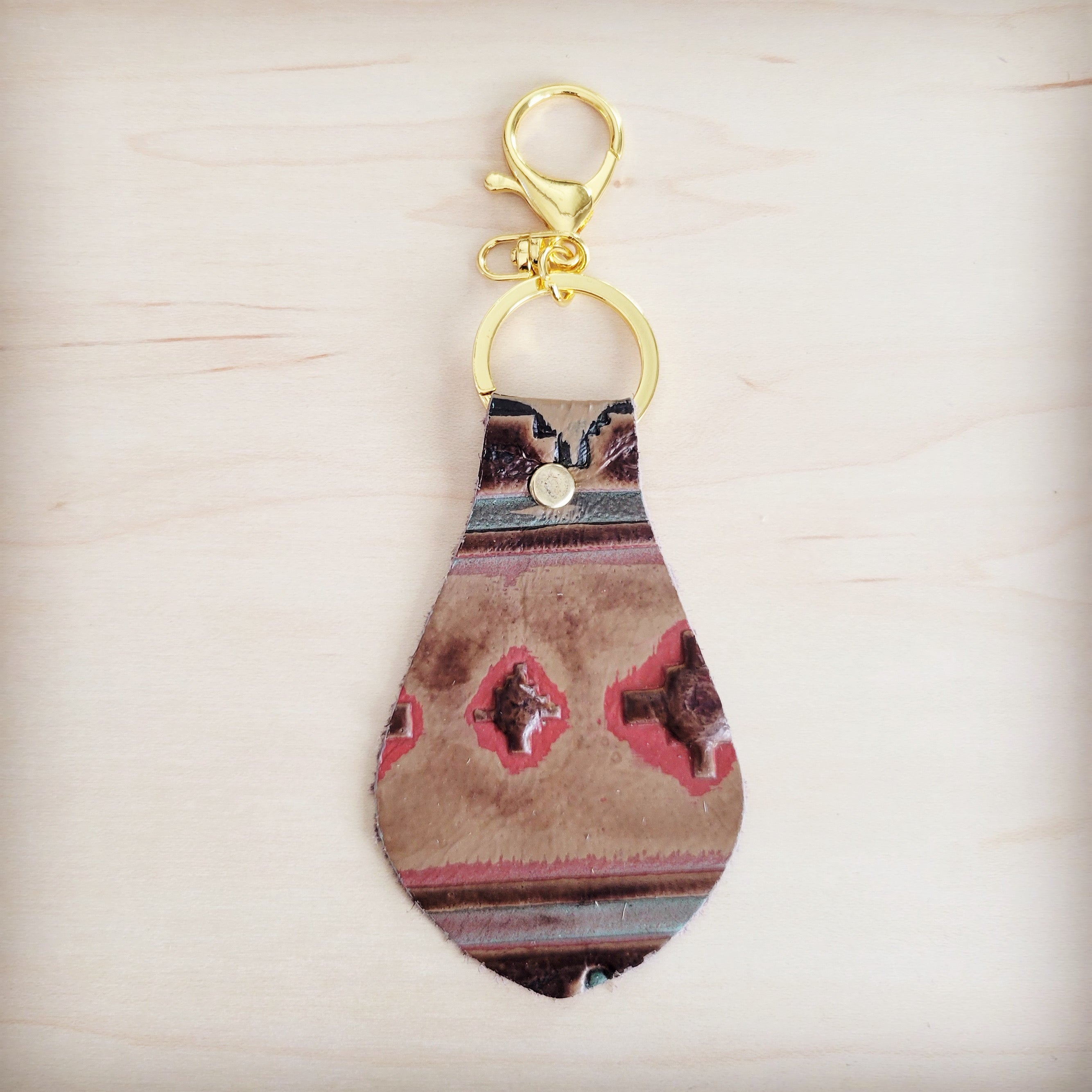 A leather keychain with a red and brown Navajo-inspired geometric print and gold-tone metal hardware against a light wooden background.