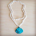 Long white turquoise beaded necklace featuring a large, vibrant blue turquoise regalite slab pendant on a wooden background