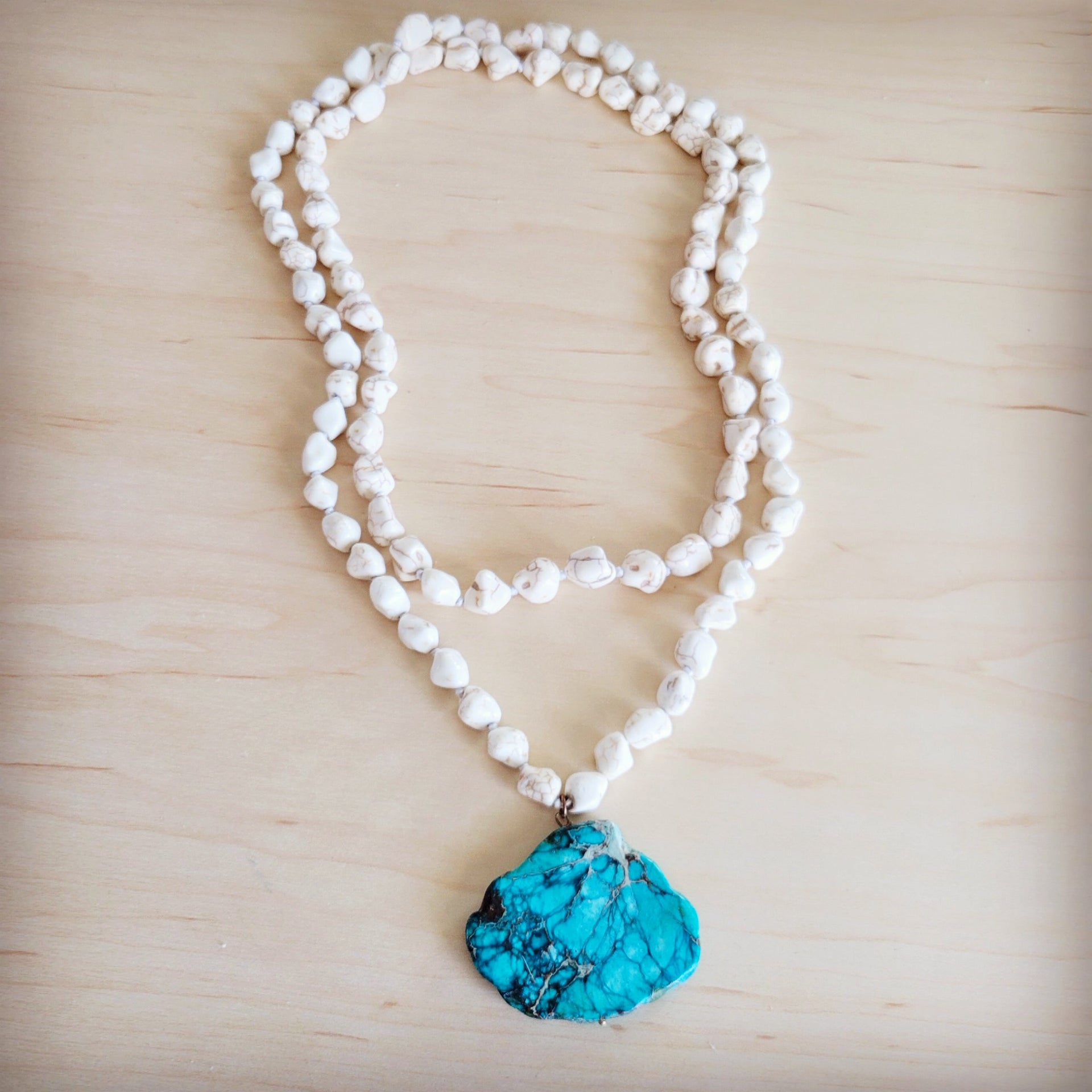 Long white turquoise beaded necklace featuring a large, vibrant blue turquoise regalite slab pendant on a wooden background