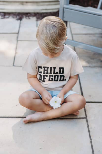 A person wearing a minimalist Child of God unisex crew neck cotton tee in black or cream.