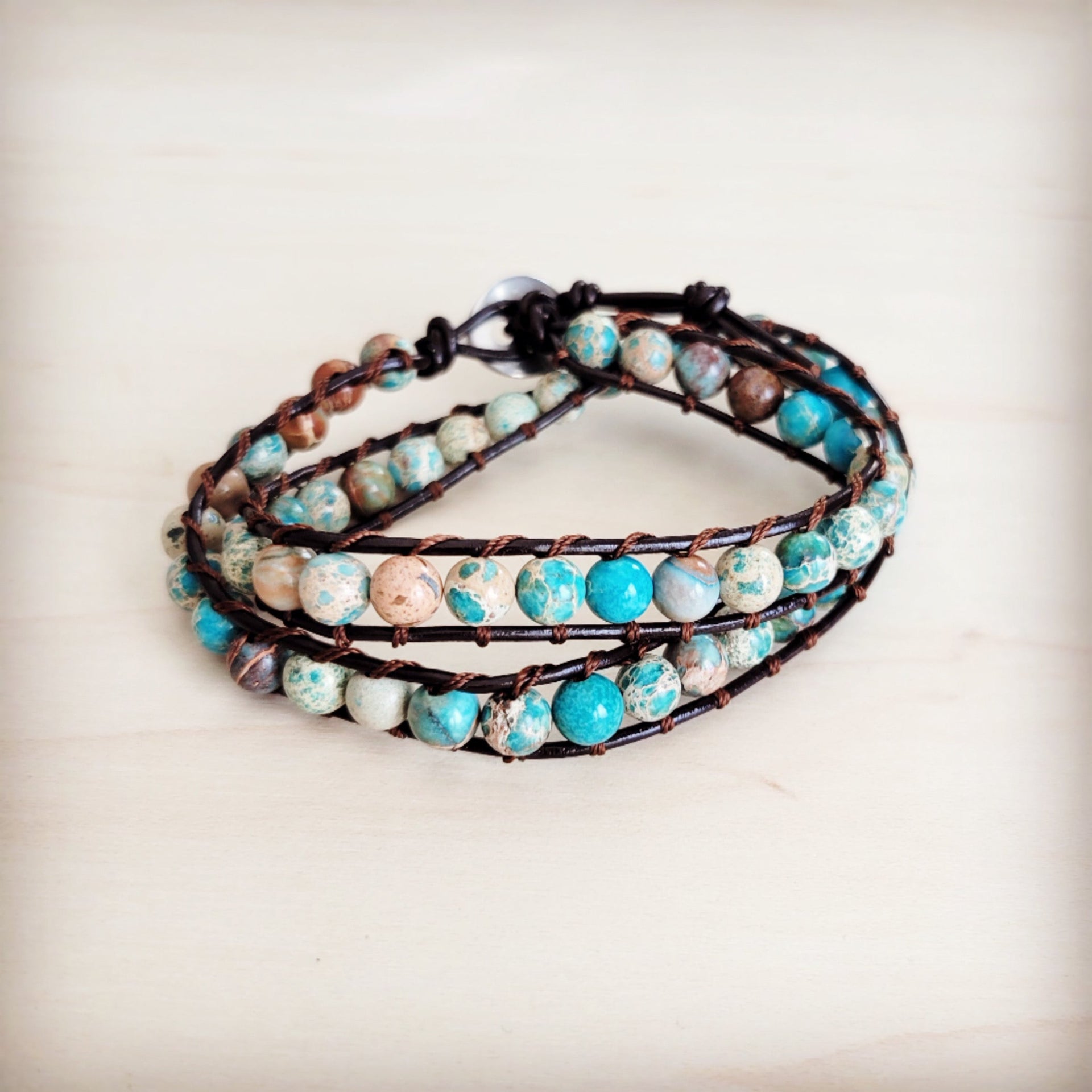 Double wrap bracelet featuring blue and earth-toned Imperial Jasper beads on a dark leather cord worn on a wrist