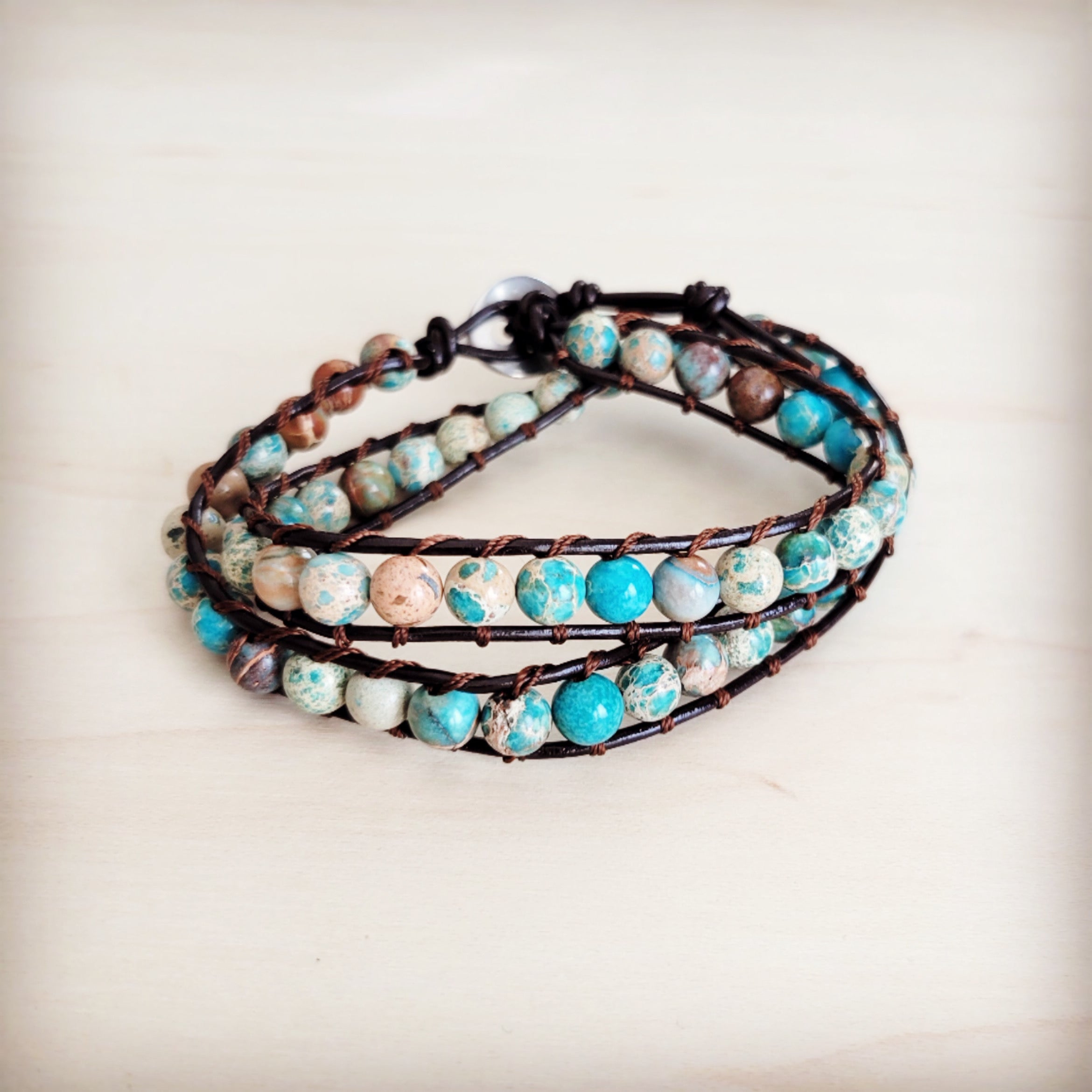 Double wrap bracelet featuring blue and earth-toned Imperial Jasper beads on a dark leather cord worn on a wrist