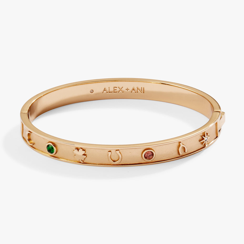 Gold tone hinge bangle bracelet with horseshoe, wishbone, and clover charms.