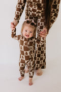 Child wearing Gingerbread Checkerboard bamboo zip pajamas in brown and cream checkerboard pattern.