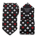 Close up of a black necktie featuring a repeating pattern of white and red playing card suits, with a hidden message on the back
