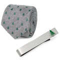 Gray herringbone necktie with small green Christmas tree pattern paired with a silver tie bar featuring a matching tree icon, displayed in a gift box.