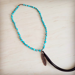 Turquoise necklace with an ornate copper feather pendant and tassel, reflecting a western boho style.
