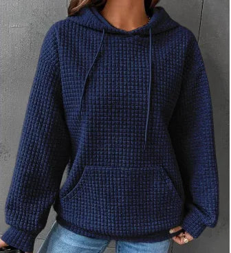A woman wearing a loose-fit long sleeve waffle knit hoodie with a front kangaroo pocket.