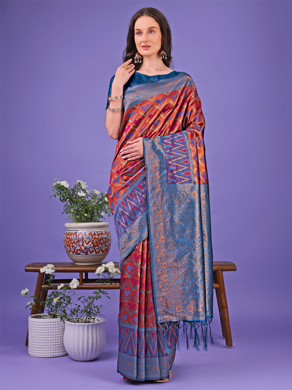 Woman wearing a Radiant Lichi Silk Saree with geometric patterns in deep-red, teal-blue, and gold.