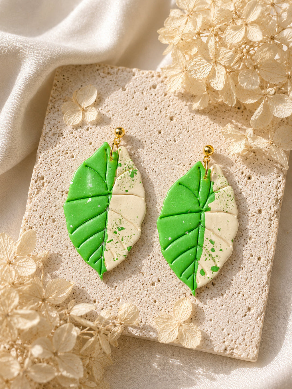 Handmade polymer clay earrings featuring a green and cream Alocasia Scabriuscula Albo variegated leaf pattern.