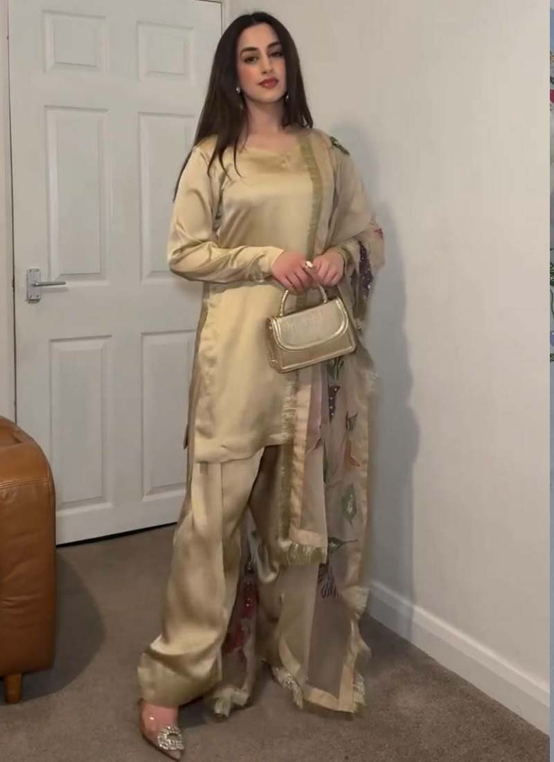 Woman wearing a golden satin silk palazzo suit with vibrant floral embroidery and a wide-leg silhouette.