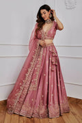 Woman wearing an onion-pink Japan Satin Silk lehenga choli with gold Zari and sequins embroidery.