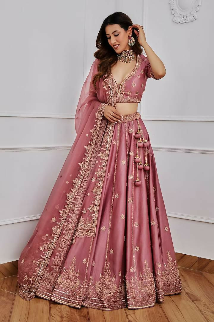 Woman wearing an onion-pink Japan Satin Silk lehenga choli with gold Zari and sequins embroidery.