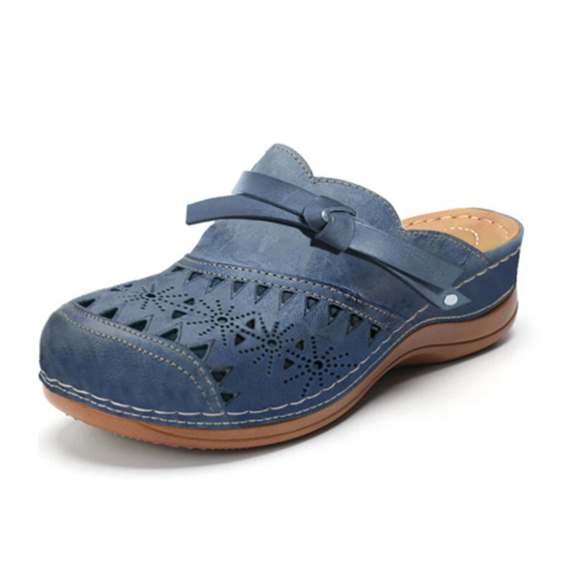Close-up of a women's blue perforated faux leather flat sandal with a decorative bow on the top, showcasing the intricate laser-cut pattern and comfortable design.