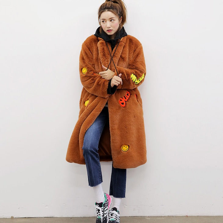 Woman wearing a brown long sleeve faux fur teddy coat with colorful embroidered smiley faces and 'FUN' patches, styled for Harajuku fashion.