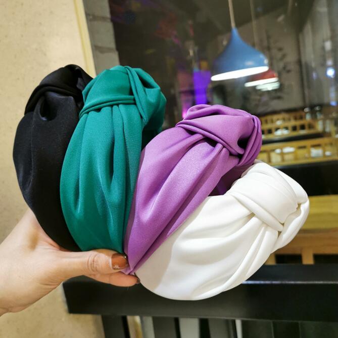 A stylish wide solid color knot headband for women, available in black, emerald green, purple, and white options.
