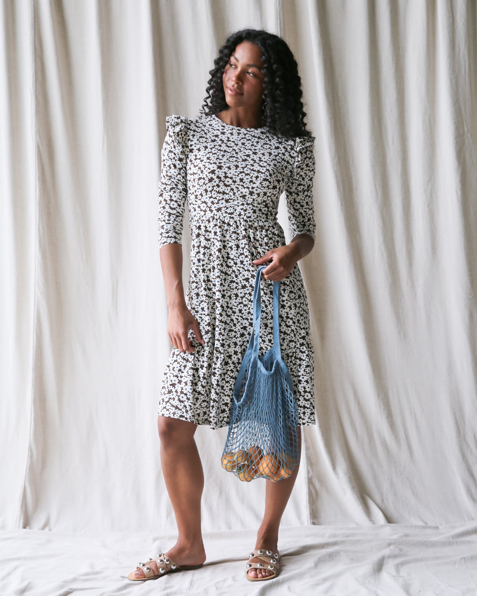 A woman wearing a floral print A-line midi dress with flutter sleeves and scoop neckline.
