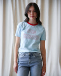 Women wearing a light blue Sun Kissed graphic t-shirt with red crew neck trim.