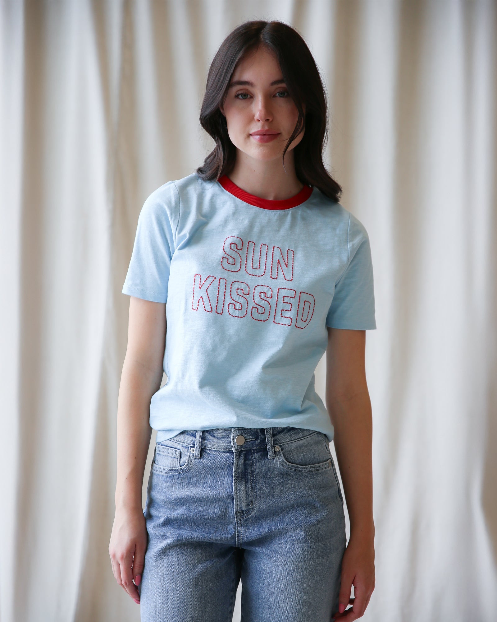 Women wearing a light blue Sun Kissed graphic t-shirt with red crew neck trim.