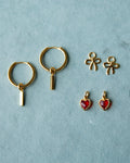 Gold huggie hoop earrings with interchangeable red heart, bow, and bar charms on a white background.