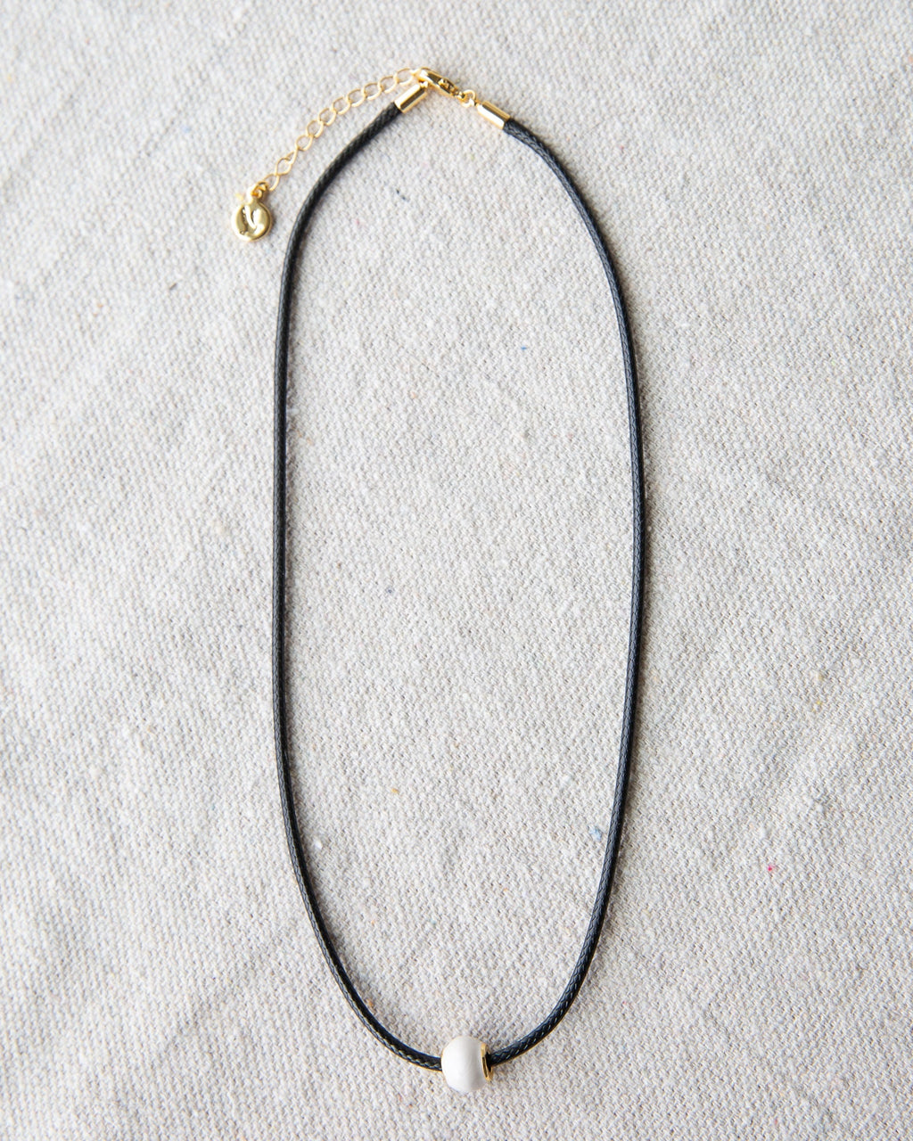 Minimalist dark brown cord choker necklace with a round glass pearl and gold-plated accents