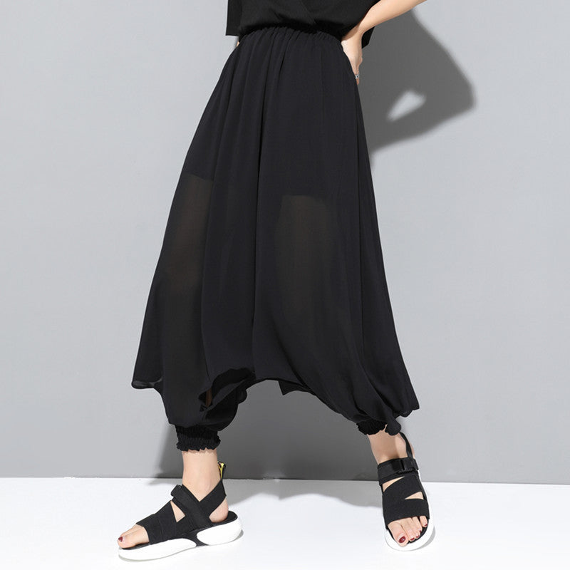 A model wearing Harajuku Style black chiffon harem pants with an elastic waist and gathered ankles, paired with black and white sandals.