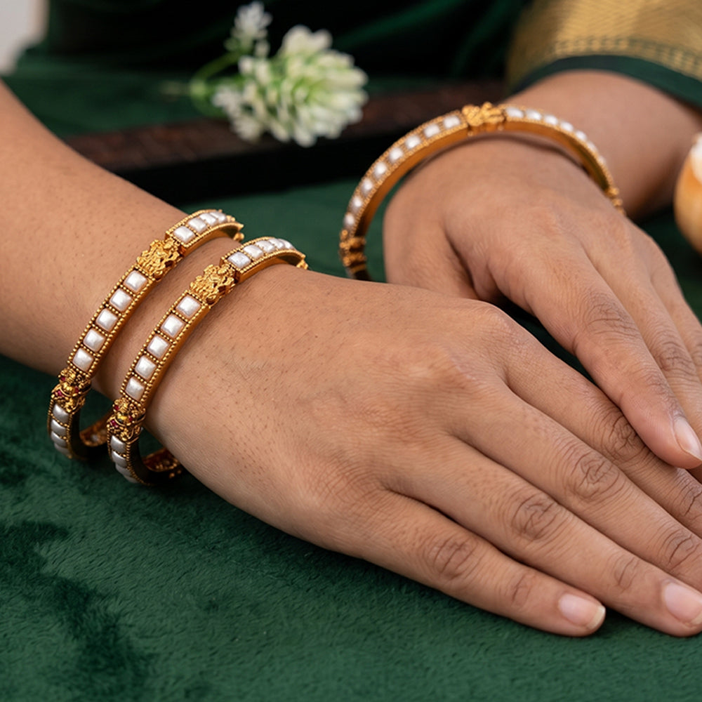 Close-up of temple design gold-finished bangles adorned with elegant pearls.