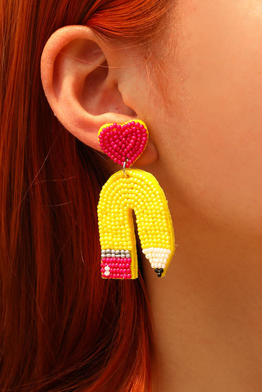Close-up of a model wearing yellow heart and pencil-shaped beaded drop earrings.