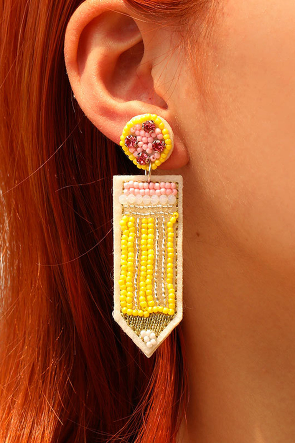 A close-up view of a person wearing yellow pencil-shaped beaded statement earrings.