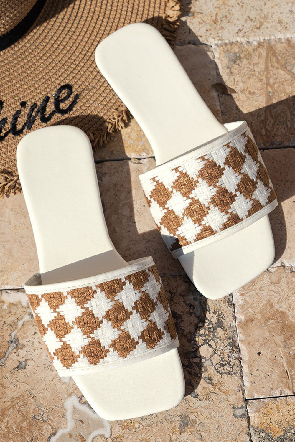 A pair of woven brown and white plaid flat sandals with a modern square-toe design shown on a patio.