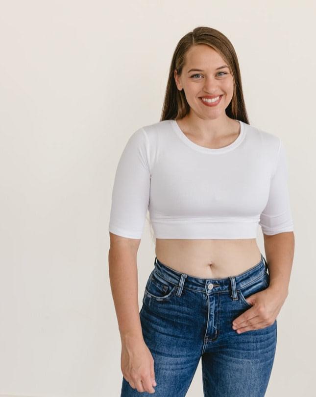 A woman wearing a white crew neck cropped layering t-shirt with elbow sleeves, paired with jeans.