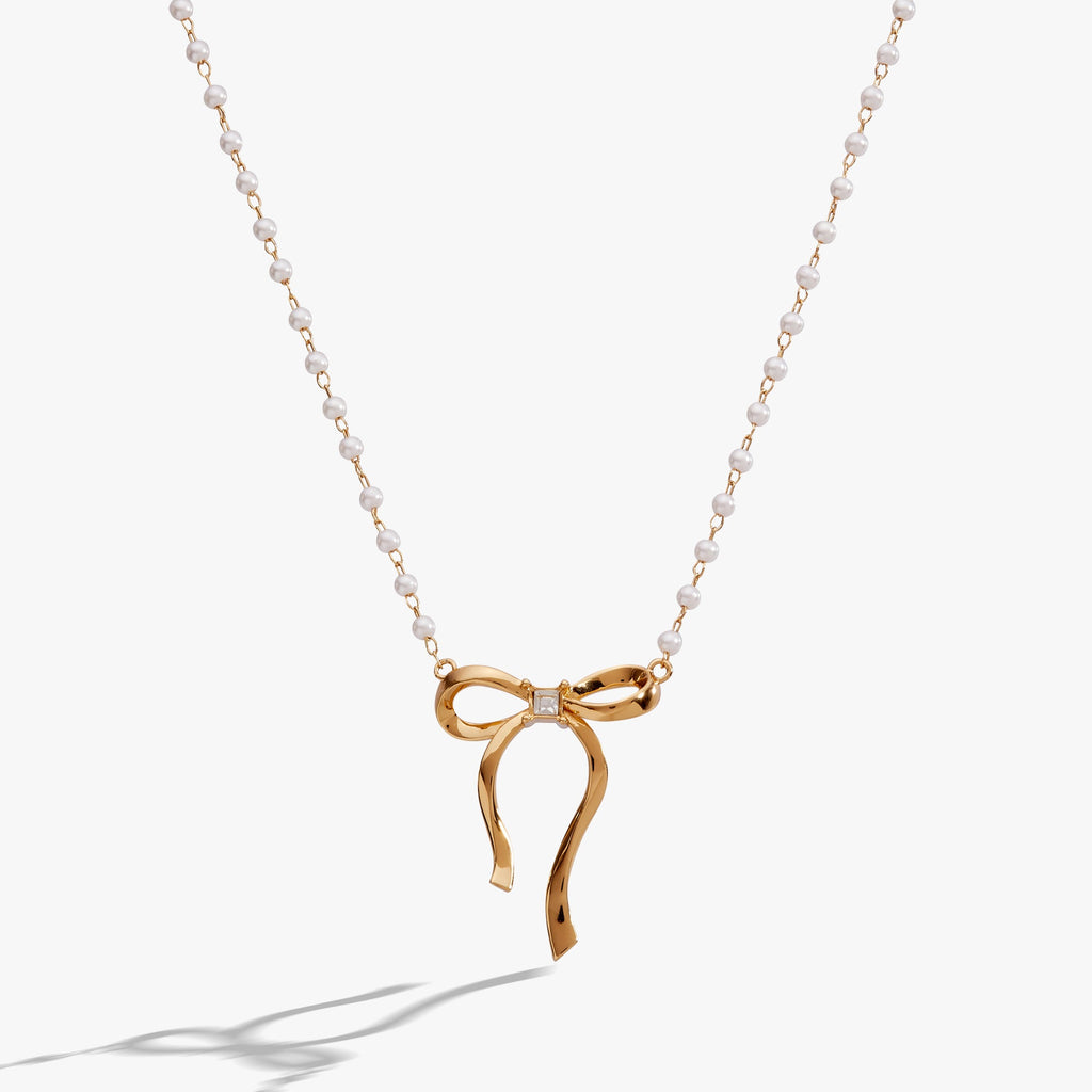White pearl bead necklace with a gold-plated bow and crystal centerpiece on a rosary chain