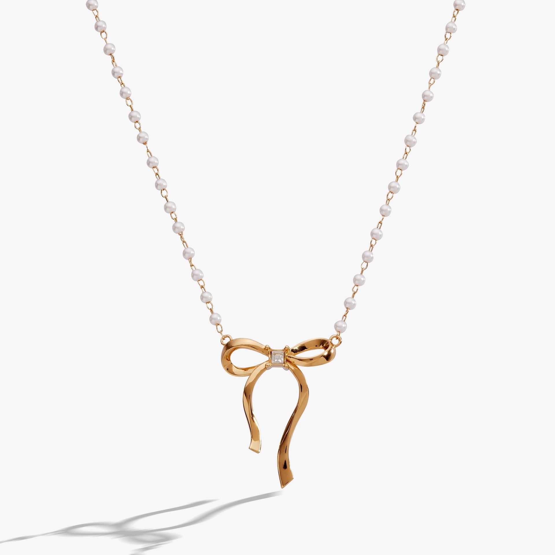 White pearl bead necklace with a gold-plated bow and crystal centerpiece on a rosary chain