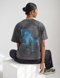 Model wearing a charcoal grey oversized heavyweight tee with slate blue graphic print, styled for a streetwear look.
