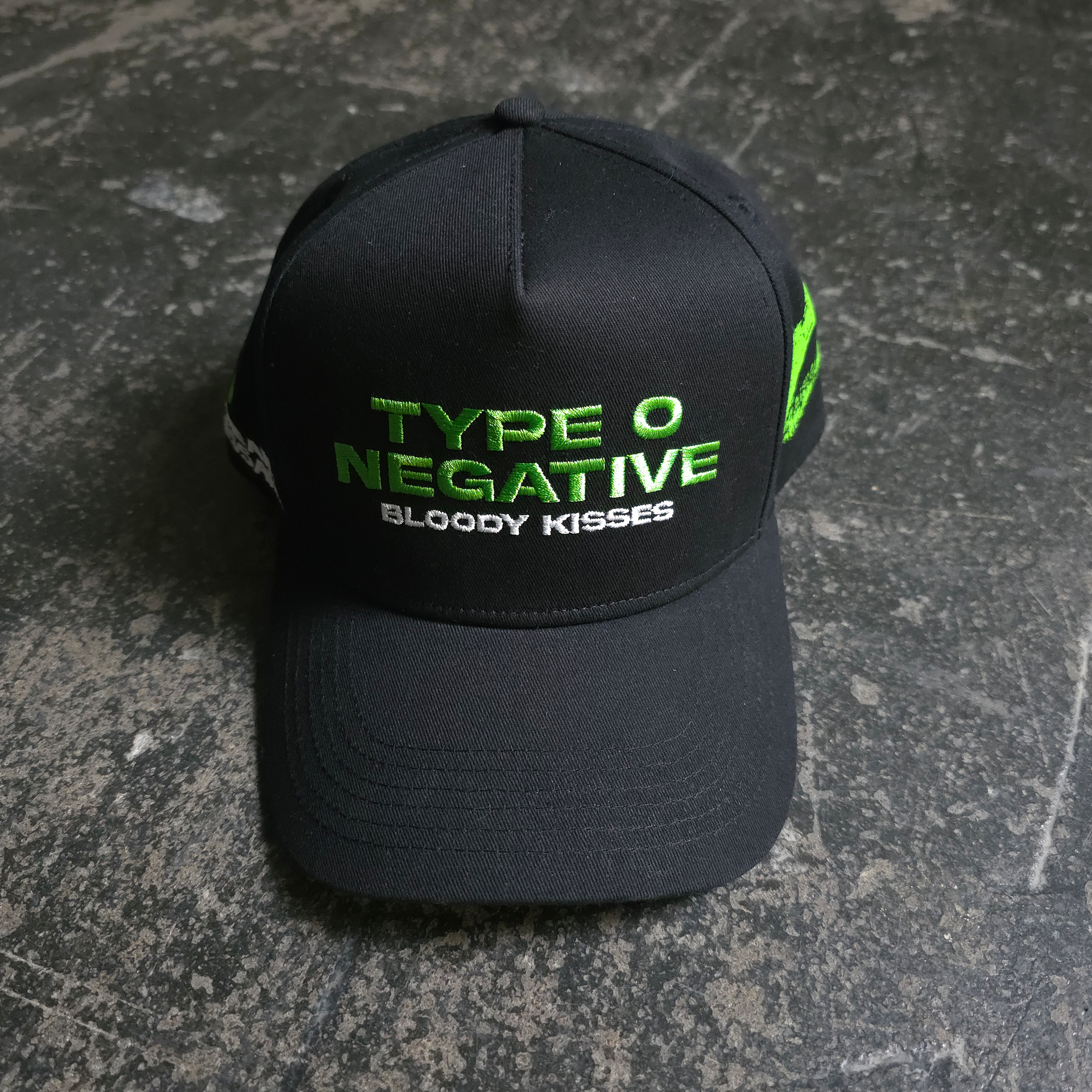 A black baseball-style cap with lime green embroidered Type O Negative and Bloody Kisses text on the front and a green kiss graphic on the side.