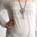 Close-up of a hand-crafted bohemian macrame and crochet pendant necklace in neutral grey and tan tones.