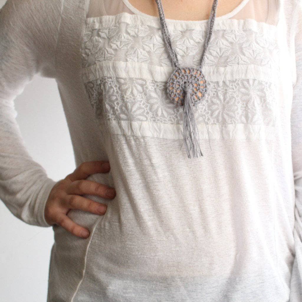 Close-up of a hand-crafted bohemian macrame and crochet pendant necklace in neutral grey and tan tones.
