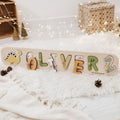 Neutral-toned dinosaur-shaped wooden name puzzle for children in beige, green, and yellow.